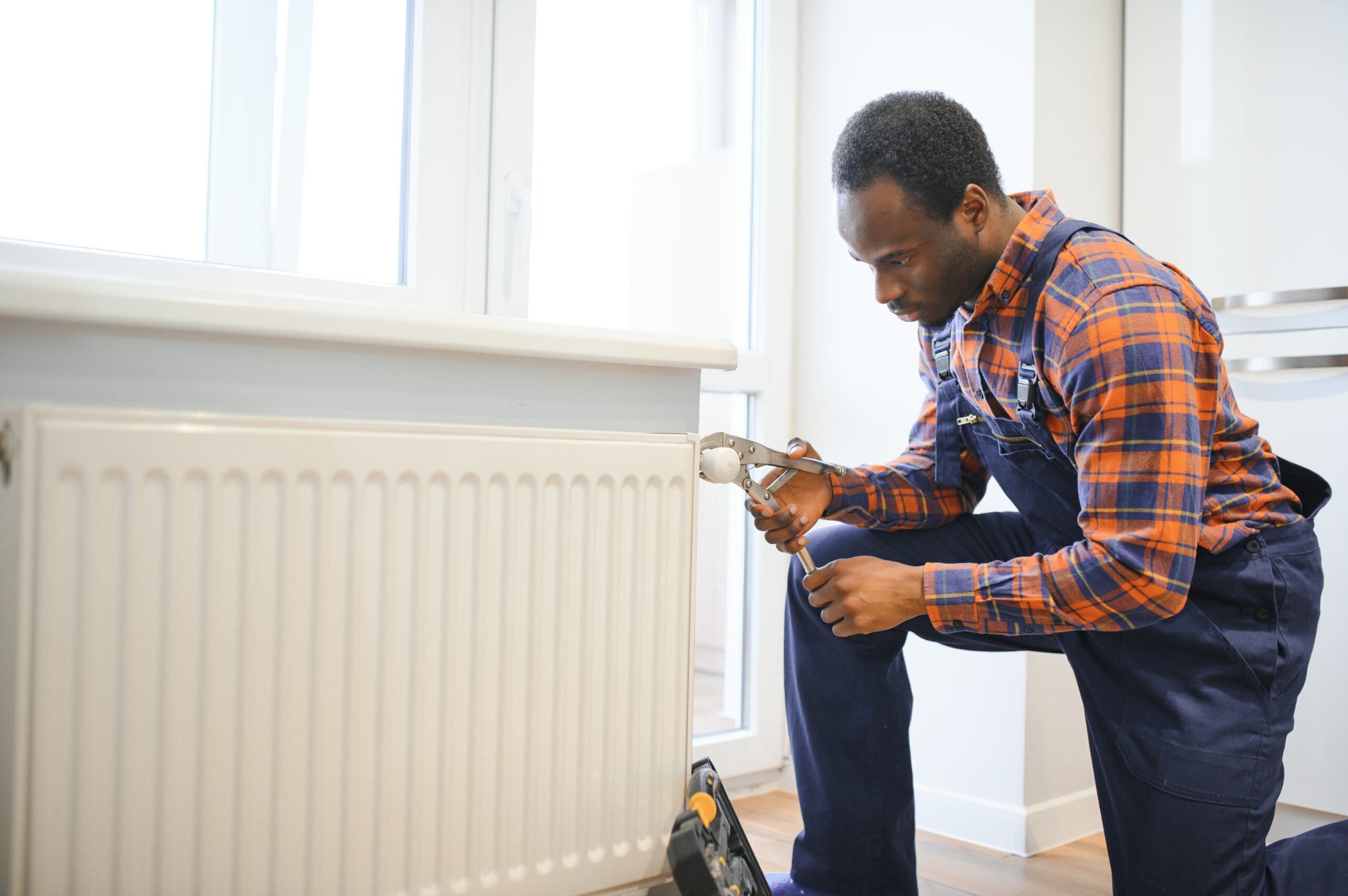 Repair heating radiator close up African man repairing radiator with wrench Removing air from the radiator